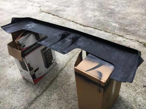 1988 Ford Bronco - A black plastic car part is resting on two cardboard boxes outdoors.