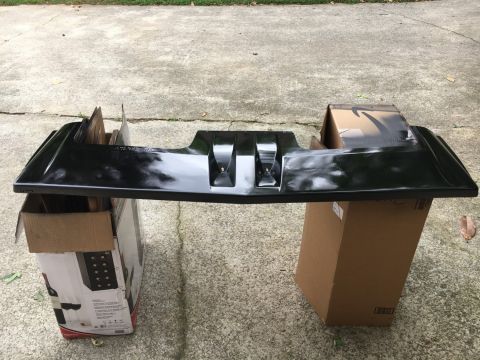 1988 Ford Bronco - Black plastic car bumper part supported by cardboard boxes on a concrete surface.
