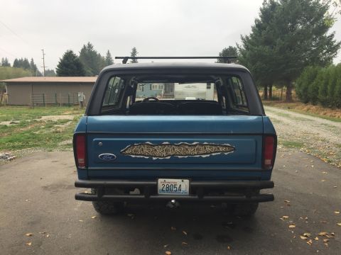 1979 Ford Bronco - This blue Ford Bronco features a camouflage decal on its tailgate and a roof rack, parked outdoors.