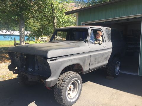 1978 Ford Bronco - A young child looks out the window of a gray 1978 Ford Bronco parked in front of a garage.
