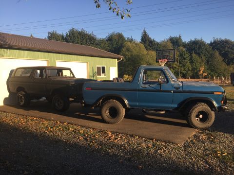 1978 Ford Bronco - A blue 1978 Ford Bronco pickup truck is parked next to a dark SUV in front of a garage.