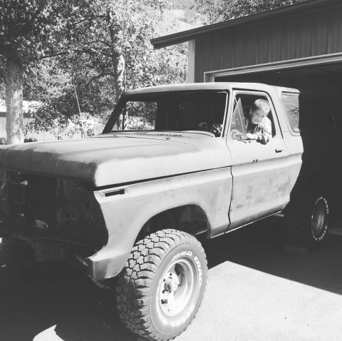 1978 Ford Bronco - A young boy sits behind the wheel of a classic Ford Bronco, parked in front of an open garage.