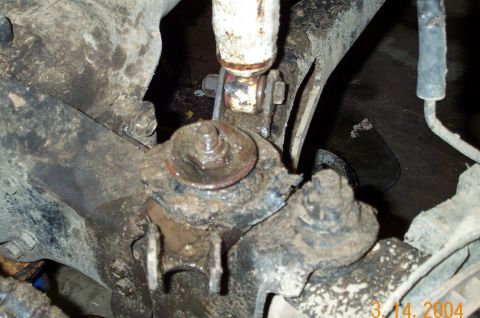 1986 Ford Bronco - Underbody close-up of a greasy, mud-caked front suspension joint, a ball joint or steering knuckle stud with a torn boot packed in grease,…