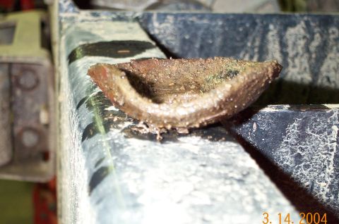 1986 Ford Bronco - Extreme close-up of a small, heavily corroded and pitted cup-shaped metal part, a dished seal or bearing cap covered in rust and grit, rest…