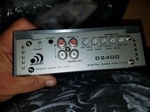 1994 Ford Bronco - A silver car stereo amplifier is held in a hand, showing its input and output connections and control knobs.