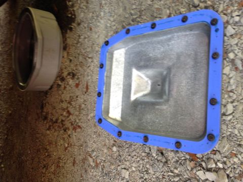 1986 Ford Bronco - Close-up of an oil pan with a blue gasket and bolts, resting on gravel.