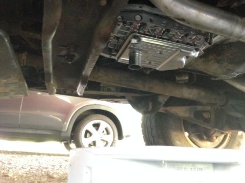 1986 Ford Bronco - The underside of a vehicle shows the transmission pan and filter, with another car parked nearby.