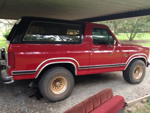 1986 Ford Bronco - This red 1986 Ford Bronco features a black removable top and is parked under a covered area.