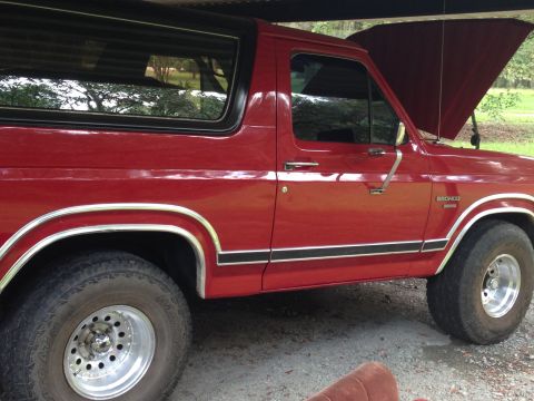 1986 Ford Bronco - The side profile of a red 1986 Ford Bronco shows its distinctive body style and trim.