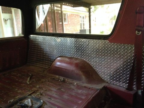 1986 Ford Bronco - The interior of a red SUV shows diamond plate paneling and a worn cargo floor.