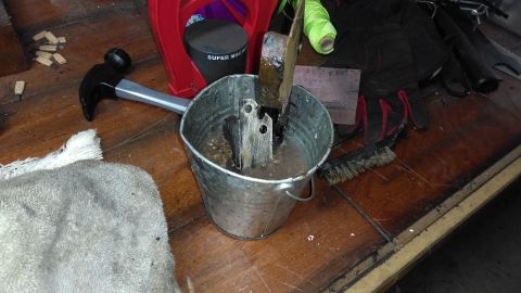 1996 Ford Bronco - A metal component is submerged in a bucket of liquid, with various tools scattered around the workbench.