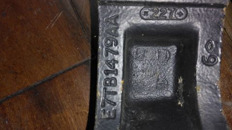 1996 Ford Bronco - A black metal part with stamped markings is shown close-up against a wooden background.