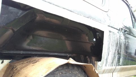 1996 Ford Bronco - Detail of a vehicle's wheel well and lower body panel, covered with protective cardboard during work.
