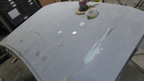 1996 Ford Bronco - Body filler is applied and sanded on a car hood in a workshop.