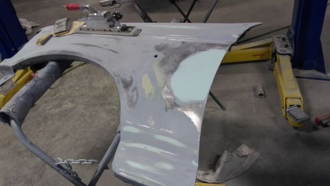 1996 Ford Bronco - A car fender is being repaired with body filler and sanding tools in a workshop.