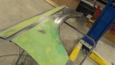 1996 Ford Bronco - A car fender, prepped with green primer and exposed metal, is held by a lift in a workshop.
