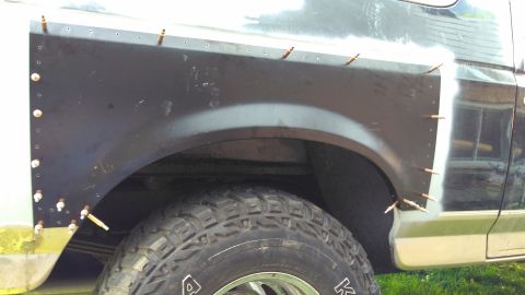 1996 Ford Bronco - A metal patch is being riveted onto the rear fender of a vehicle, indicating body repair work.