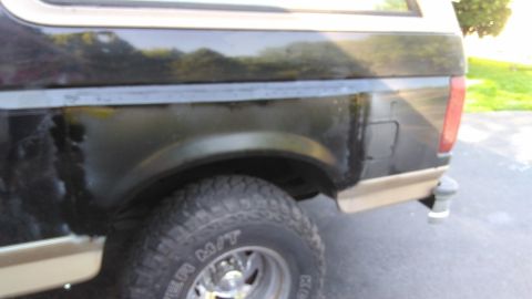 1996 Ford Bronco - The rear section of a dark-colored SUV with tan trim displays signs of wear and tear, including rust spots.