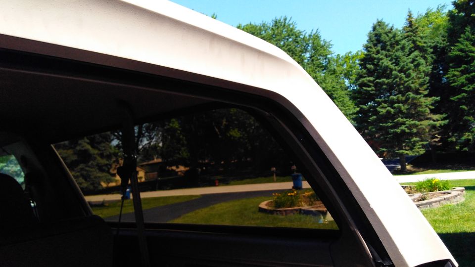 View from inside a vehicle looking out the side window at a suburban street and trees. Watermark reads SUPERMOTORS