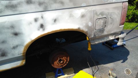1996 Ford Bronco - The rear quarter panel of a vehicle is shown with rust and primer, indicating it is undergoing body work and paint preparation.