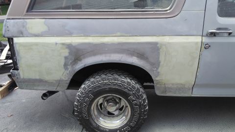 1996 Ford Bronco - The rear quarter panel of a vehicle shows extensive bodywork in progress, with primer and filler applied over damaged areas.