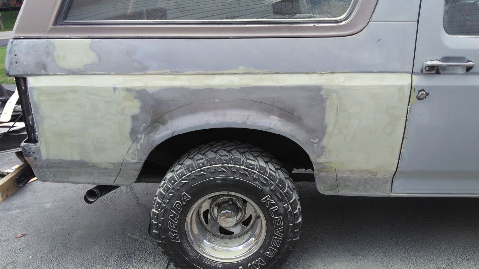 Side view of vehicle's rear quarter panel with body filler and primer