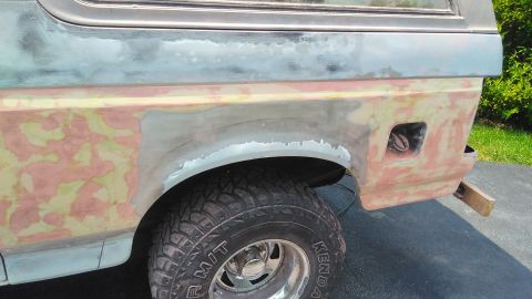 1996 Ford Bronco - The rear quarter panel of a Ford Bronco is shown with primer and filler, indicating repair work is in progress.
