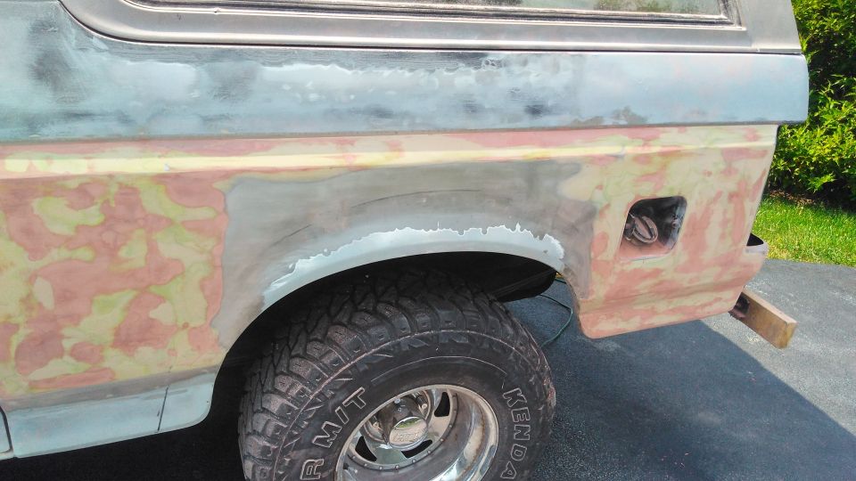 Rear quarter panel of a Ford Bronco undergoing bodywork, showing primer and filler