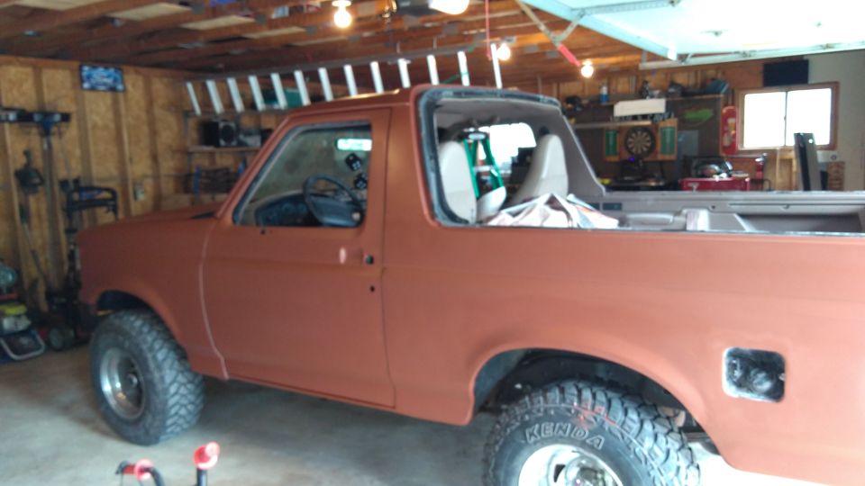 Orange 1996 Ford Bronco side view in garage, undergoing paint work