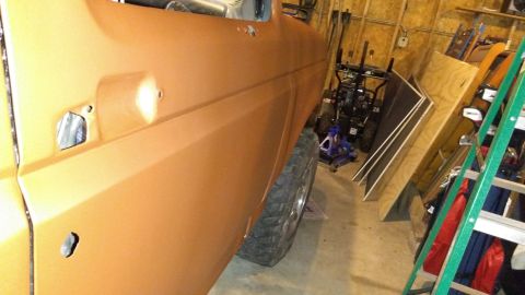 1996 Ford Bronco - Side view of an orange vehicle's door and wheel well in a cluttered garage.