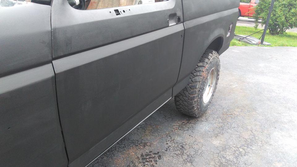 1996 Ford Bronco side panel with primer, showing front door seam and rear fender. Off-road tire visible