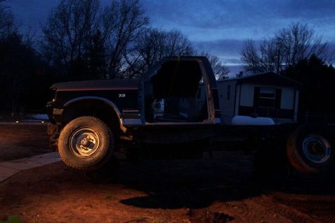 1990 Ford Bronco - Side view of a 1990s Ford F-Series truck chassis with its cab intact, parked outdoors.