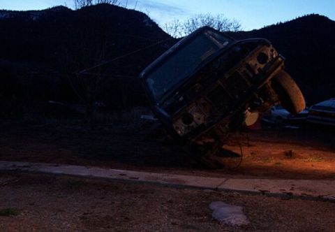 1990 Ford Bronco - An overturned vehicle rests precariously on its side in a rural area at dusk.
