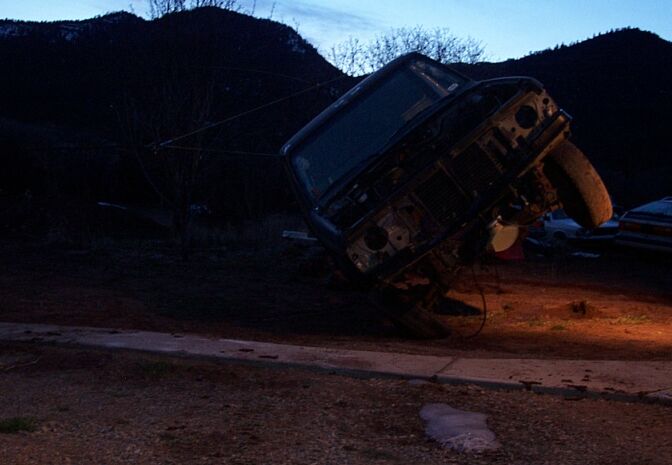 Gutted truck cab tipped on its side at dusk, exposed grille and radiator support