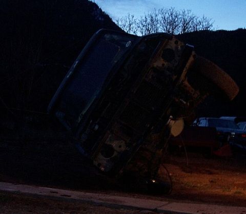 1990 Ford Bronco - An overturned 1990 Ford Bronco lies on its side at dusk, with other vehicles visible in the background.
