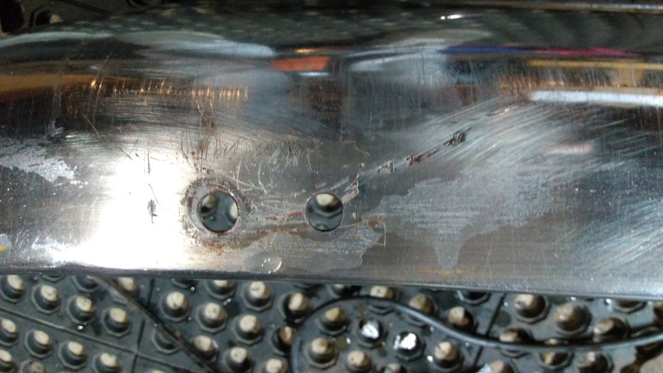 Close-up of a scratched chrome bumper with two bolt holes