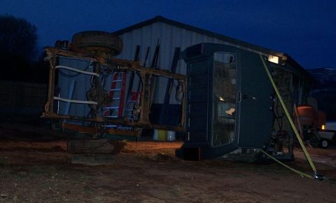 1990 Ford Bronco - A dark green truck cab and chassis lies on its side next to a building, revealing its internal structure and a ladder.