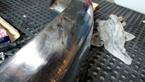 1996 Ford Bronco - Close-up of a chrome bumper with visible wear and tear, next to a cleaning rag.