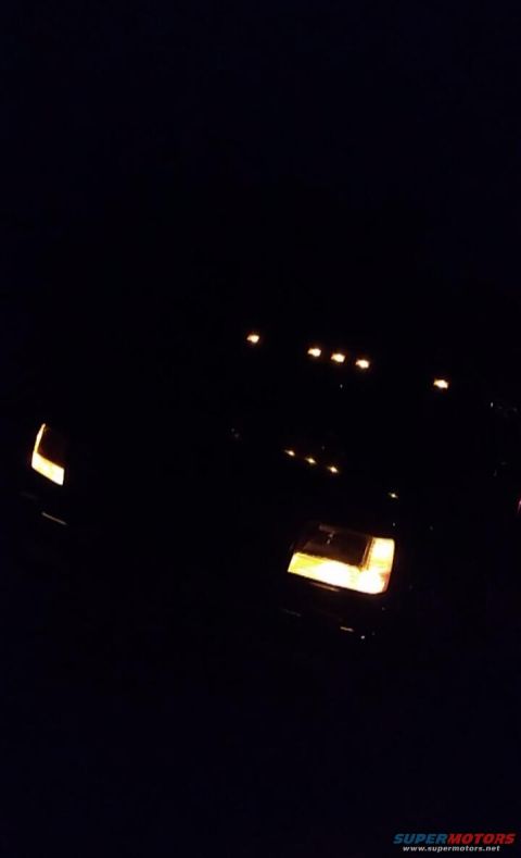 1996 Ford Bronco - The front of a black 1996 Ford Bronco is visible at night, with its headlights and roof marker lights on.