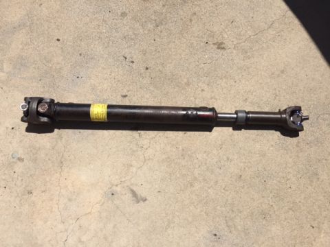 1978 Ford Bronco - A driveshaft is shown resting on a concrete surface, a yellow warning label and some red paint marks.