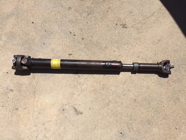 Driveshaft with yellow sticker and red markings, lying on concrete