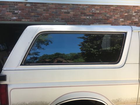 1988 Ford Bronco - Side view of a white SUV, reflecting trees and sky in its window.