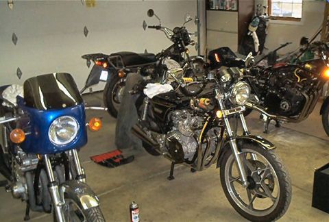 1985 Ford Crown Victoria LTD - Several motorcycles are parked in a garage, with tools and supplies visible around them.