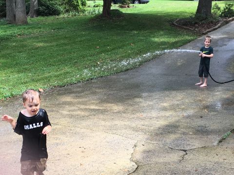 1988 Ford Bronco - Two young boys are playing with a hose on a driveway on a sunny day.