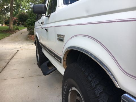 1988 Ford Bronco - Side profile of a white 1988 Ford Bronco, its distinctive body style and pinstripe detailing.