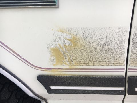 1988 Ford Bronco - Close-up of a damaged decal on the side of a vehicle, with sand and dirt obscuring the text.