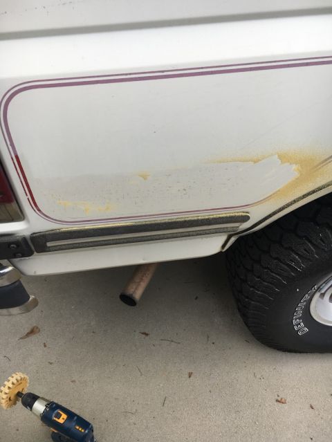 1988 Ford Bronco - Detail of a white SUV's rear side, showing trim, rust, and an exhaust pipe, with a cleaning tool nearby.