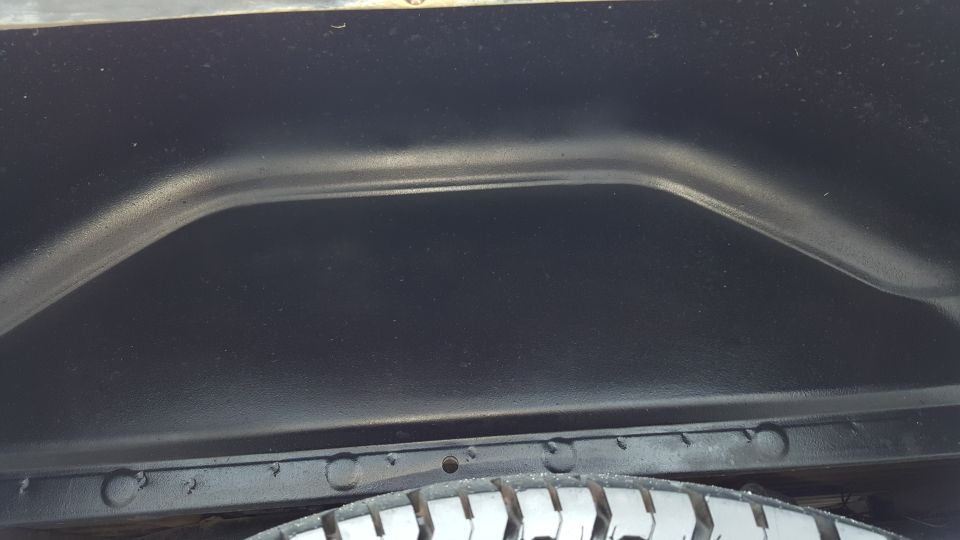 Close-up of a vehicle's rear wheel well interior with a tire visible below