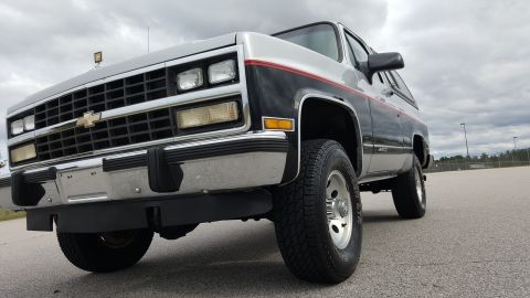 1995 Ford Bronco - This two-tone black and silver SUV is shown from a low 3/4 front angle, highlighting its chrome bumper and red side stripe.