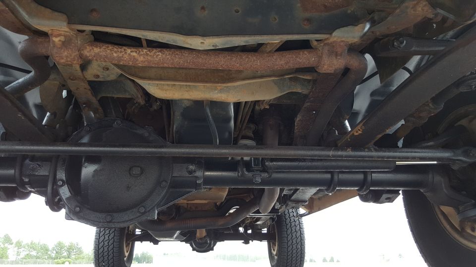 Underside view of a vehicle's drivetrain and suspension components, showing rust on some parts